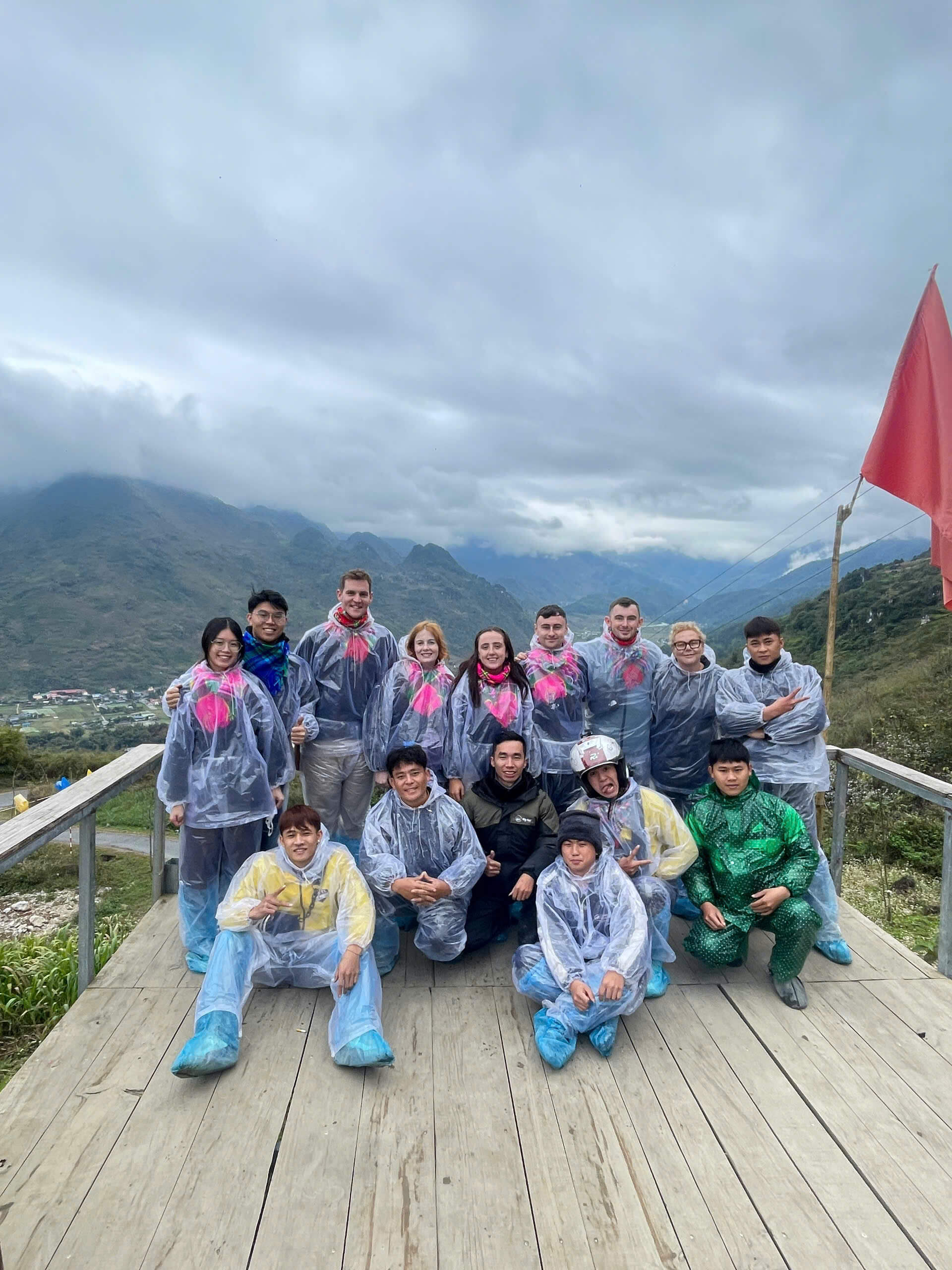 Travel group wearing colorful rain ponchos on a misty day, highlighting how to prepare for different weather conditions when deciding the best time to visit Ha Giang Loop.